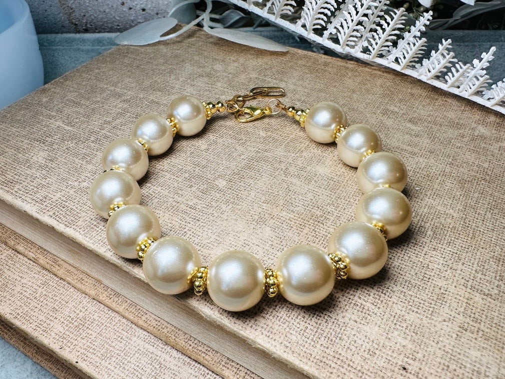 This classic pearl bracelet is handmade with gorgeous champagne pearls, gold filigree accents, and 18K hardware. The gold accents paired with the creamy champagne pearls are a classic and timeless design. This bracelet looks fantastic worn alone- or stack it with others to make a statement. This bracelet is made to order. Please select your desired base length at check out- a 1.5" extension will be added to easily customize the fit. Lobster clasp closure. A beautiful pearl bracelet- matching earrings are