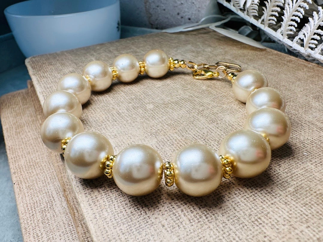 This classic pearl bracelet is handmade with gorgeous champagne pearls, gold filigree accents, and 18K hardware. The gold accents paired with the creamy champagne pearls are a classic and timeless design. This bracelet looks fantastic worn alone- or stack it with others to make a statement. This bracelet is made to order. Please select your desired base length at check out- a 1.5" extension will be added to easily customize the fit. Lobster clasp closure. A beautiful pearl bracelet- matching earrings are