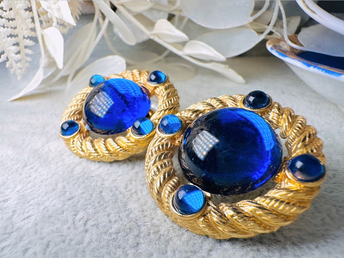 These vintage Park Lane gold rope earrings with cobalt blue cabochons are absolutely out of this world! Vibrant deep blue cabochons glow as they are surrounded by an intricate gold rope border that is accented with four more smaller blue jewels. These stones are so vibrant and vividly pop against their gold setting. Ultimate 80s mega star vibes, post style for pierced ears. Highly collectible signed designer pair in excellent vintage condition, no major flaws to note.