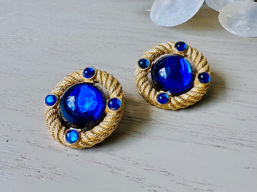 These vintage Park Lane gold rope earrings with cobalt blue cabochons are absolutely out of this world! Vibrant deep blue cabochons glow as they are surrounded by an intricate gold rope border that is accented with four more smaller blue jewels. These stones are so vibrant and vividly pop against their gold setting. Ultimate 80s mega star vibes, post style for pierced ears. Highly collectible signed designer pair in excellent vintage condition, no major flaws to note.