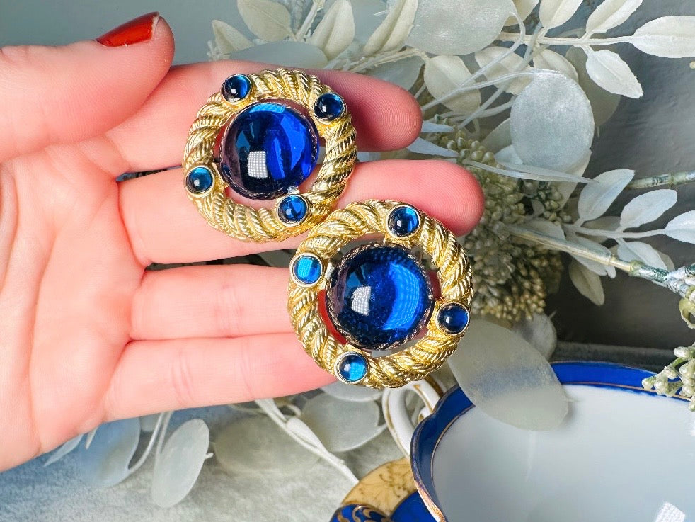These vintage Park Lane gold rope earrings with cobalt blue cabochons are absolutely out of this world! Vibrant deep blue cabochons glow as they are surrounded by an intricate gold rope border that is accented with four more smaller blue jewels. These stones are so vibrant and vividly pop against their gold setting. Ultimate 80s mega star vibes, post style for pierced ears. Highly collectible signed designer pair in excellent vintage condition, no major flaws to note.