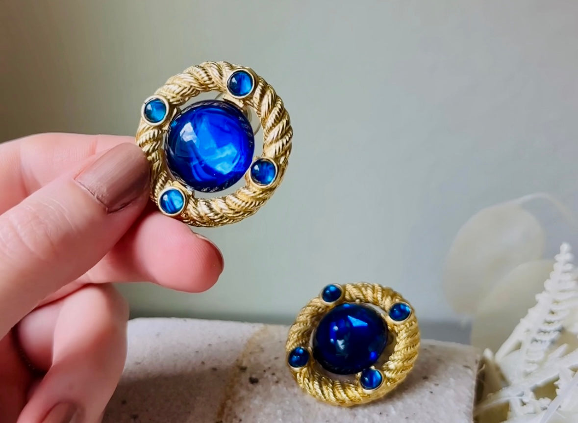 These vintage Park Lane gold rope earrings with cobalt blue cabochons are absolutely out of this world! Vibrant deep blue cabochons glow as they are surrounded by an intricate gold rope border that is accented with four more smaller blue jewels. These stones are so vibrant and vividly pop against their gold setting. Ultimate 80s mega star vibes, post style for pierced ears. Highly collectible signed designer pair in excellent vintage condition, no major flaws to note.