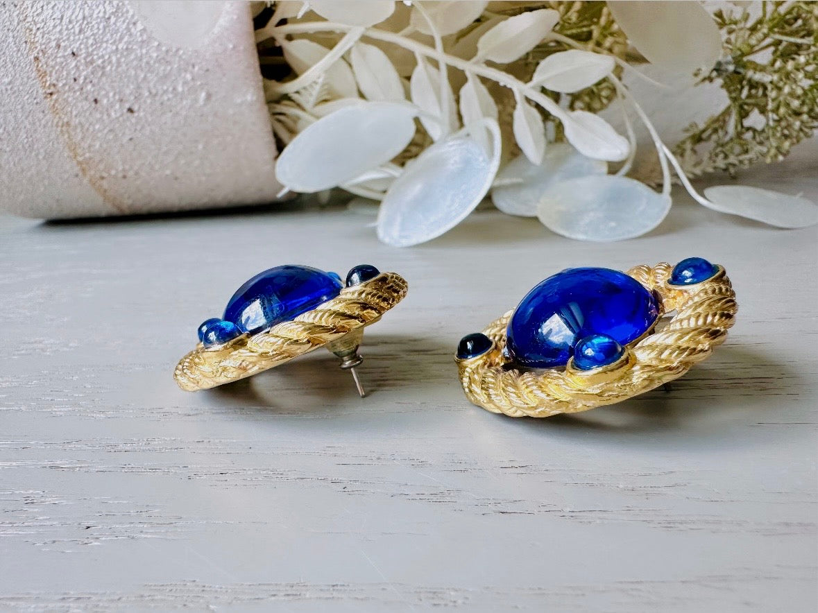These vintage Park Lane gold rope earrings with cobalt blue cabochons are absolutely out of this world! Vibrant deep blue cabochons glow as they are surrounded by an intricate gold rope border that is accented with four more smaller blue jewels. These stones are so vibrant and vividly pop against their gold setting. Ultimate 80s mega star vibes, post style for pierced ears. Highly collectible signed designer pair in excellent vintage condition, no major flaws to note.