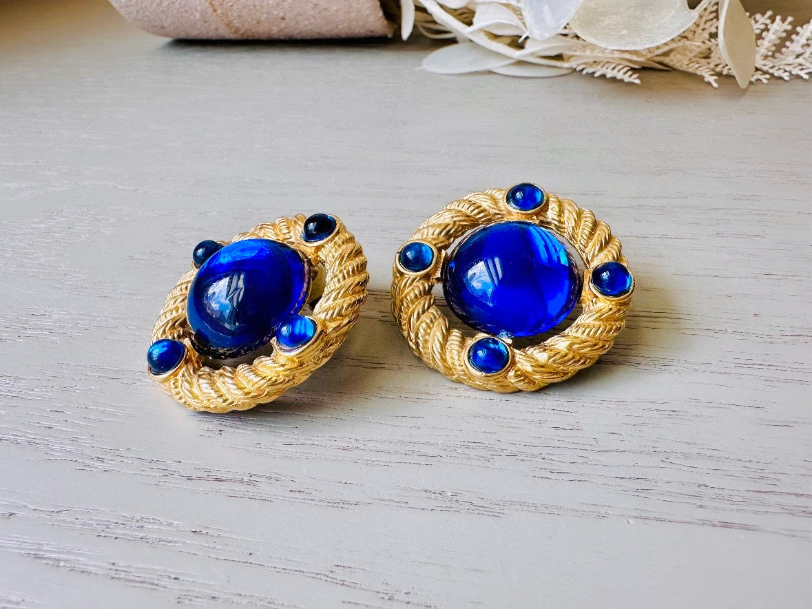 These vintage Park Lane gold rope earrings with cobalt blue cabochons are absolutely out of this world! Vibrant deep blue cabochons glow as they are surrounded by an intricate gold rope border that is accented with four more smaller blue jewels. These stones are so vibrant and vividly pop against their gold setting. Ultimate 80s mega star vibes, post style for pierced ears. Highly collectible signed designer pair in excellent vintage condition, no major flaws to note.