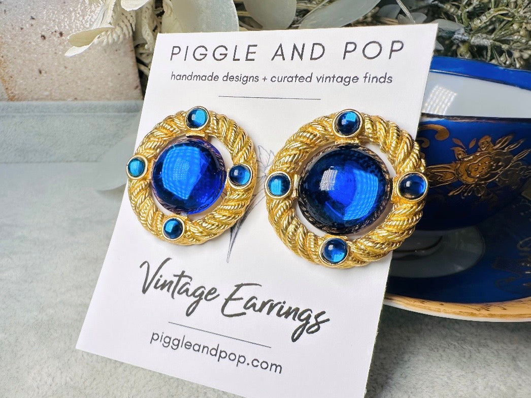 These vintage Park Lane gold rope earrings with cobalt blue cabochons are absolutely out of this world! Vibrant deep blue cabochons glow as they are surrounded by an intricate gold rope border that is accented with four more smaller blue jewels. These stones are so vibrant and vividly pop against their gold setting. Ultimate 80s mega star vibes, post style for pierced ears. Highly collectible signed designer pair in excellent vintage condition, no major flaws to note.