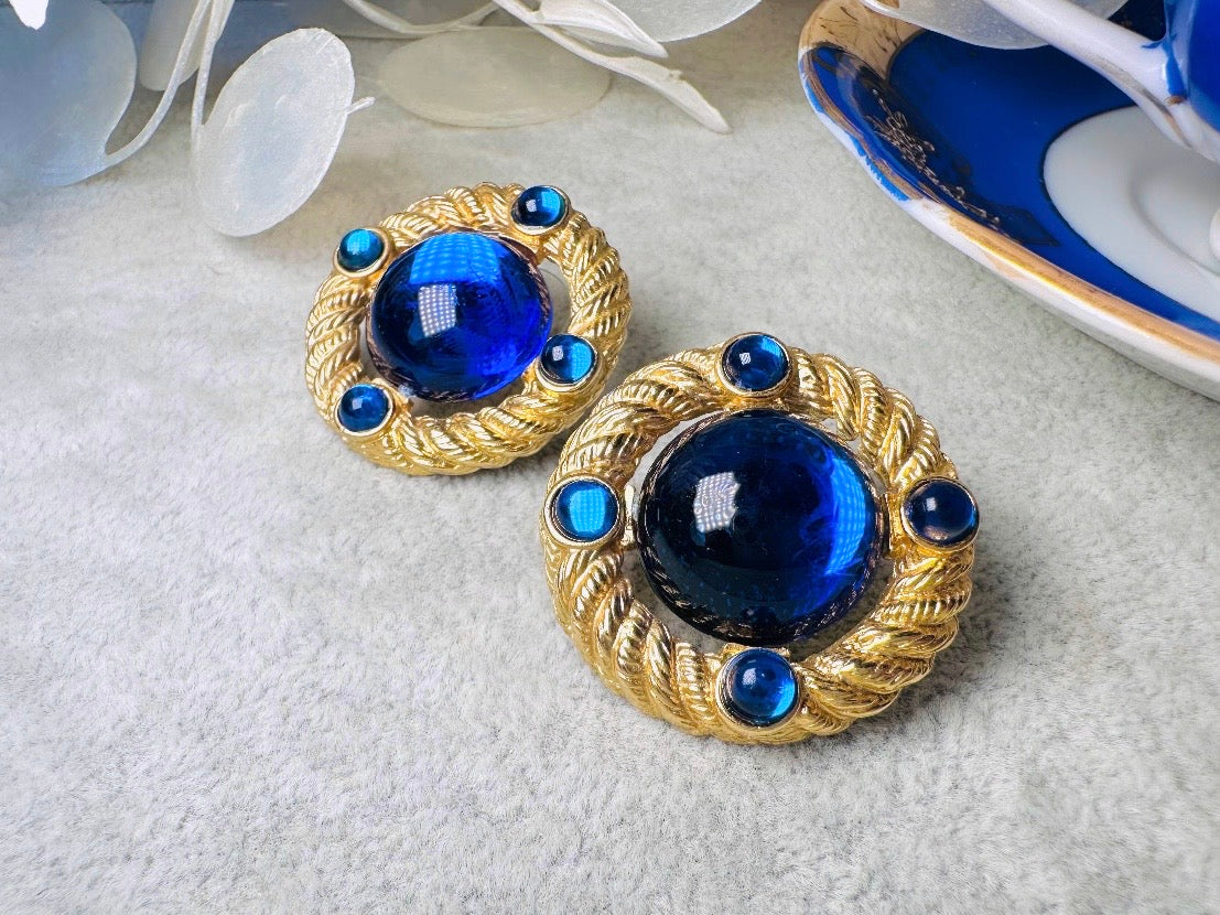 These vintage Park Lane gold rope earrings with cobalt blue cabochons are absolutely out of this world! Vibrant deep blue cabochons glow as they are surrounded by an intricate gold rope border that is accented with four more smaller blue jewels. These stones are so vibrant and vividly pop against their gold setting. Ultimate 80s mega star vibes, post style for pierced ears. Highly collectible signed designer pair in excellent vintage condition, no major flaws to note.