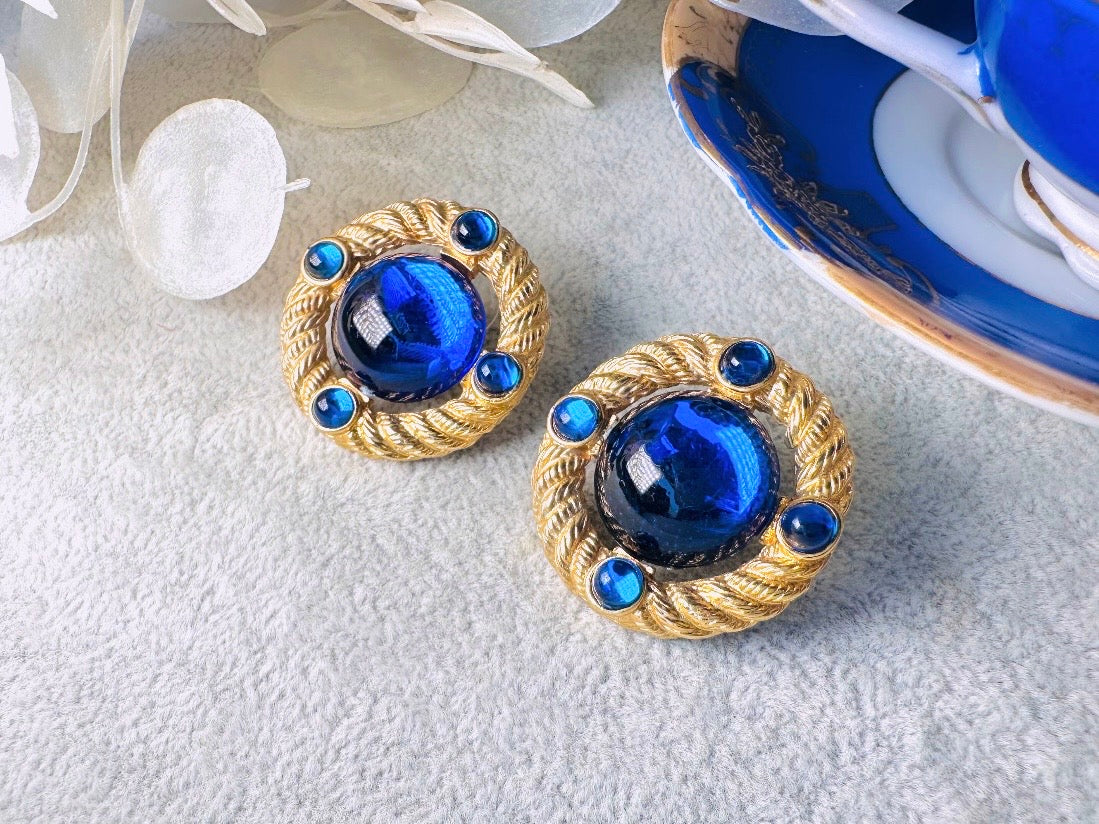 These vintage Park Lane gold rope earrings with cobalt blue cabochons are absolutely out of this world! Vibrant deep blue cabochons glow as they are surrounded by an intricate gold rope border that is accented with four more smaller blue jewels. These stones are so vibrant and vividly pop against their gold setting. Ultimate 80s mega star vibes, post style for pierced ears. Highly collectible signed designer pair in excellent vintage condition, no major flaws to note.