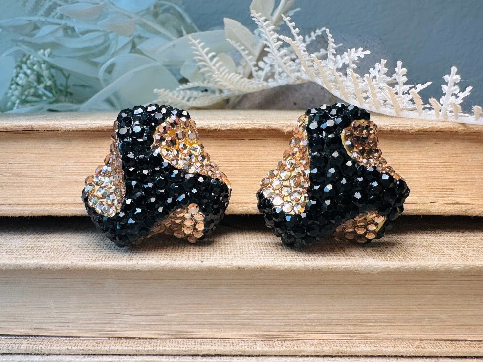 These glamorous vintage Richard Kerr cocktail earrings are spectacular. Sparkling black and gold pave set Swarovski crystals cover the entirety of the earrings, these statement earrings are the height of 80s glam. Featuring a sculptural 3d shape like a knot. The gold component is a rich topaz hue.
Clip on style, in great vintage condition.