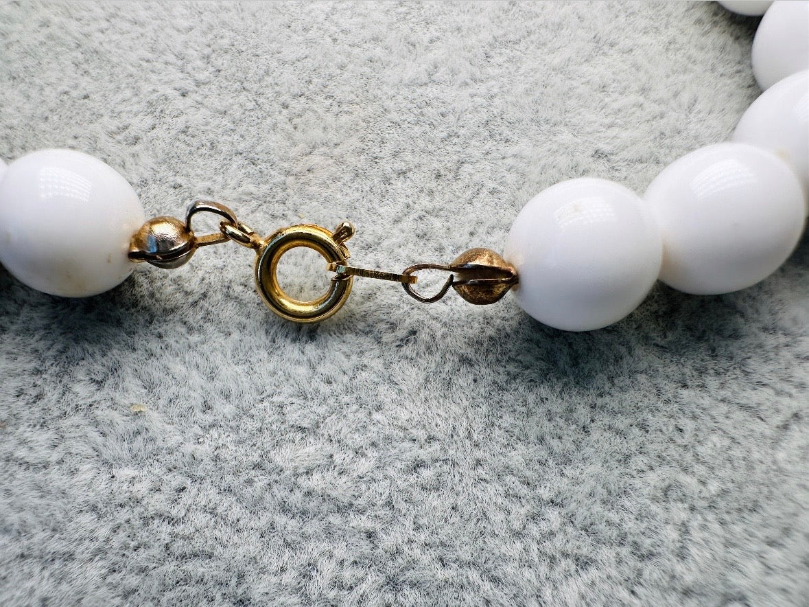 This vintage necklace is a classic. Featuring a graduated design with large, glossy marbled beads in a soft ivory-yellow hue as the focal points. These beads have a semi-translucent quality with swirling patterns that give them a unique appearance. Between the larger marbled beads are smaller, lustrous faux pearl beads and opaque white round beads, adding contrast and a touch of classic sophistication. The beads are symmetrically arranged, with the largest marbled beads positioned centrally, gradually trans