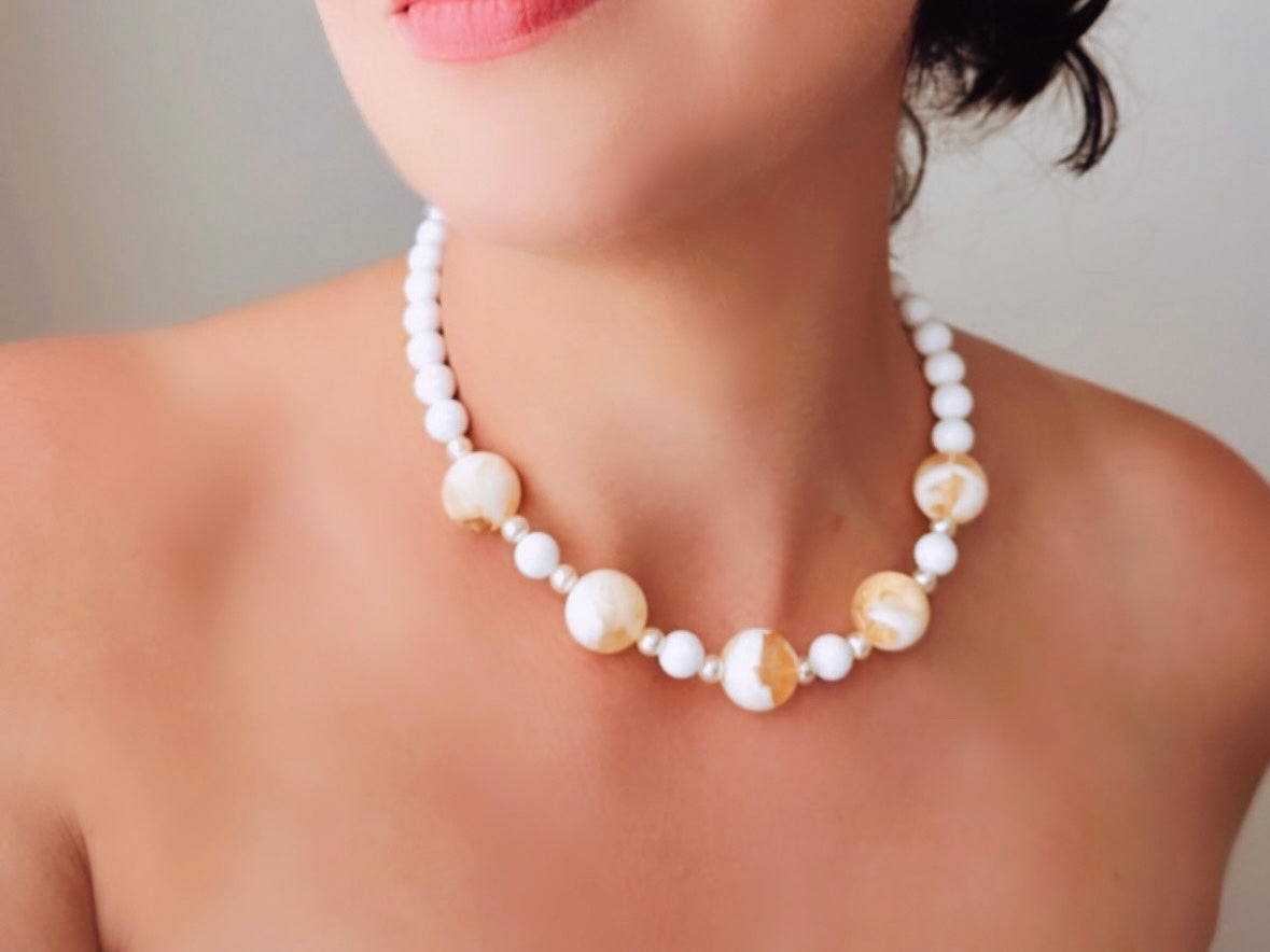This vintage necklace is a classic. Featuring a graduated design with large, glossy marbled beads in a soft ivory-yellow hue as the focal points. These beads have a semi-translucent quality with swirling patterns that give them a unique appearance. Between the larger marbled beads are smaller, lustrous faux pearl beads and opaque white round beads, adding contrast and a touch of classic sophistication. The beads are symmetrically arranged, with the largest marbled beads positioned centrally, gradually trans