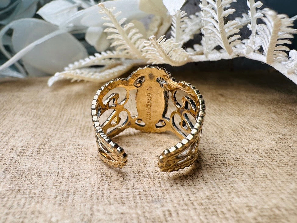 This 1970s Victorian revival vintage filigree ring is gorgeous. Featuring a faux fire opal cabochon stone set in a gold dotted bezel, the base of the ring is a beautiful open work lace filigree in an antique gold. High quality and strong filigree. Marked Sarah Coventry from 1970s.
