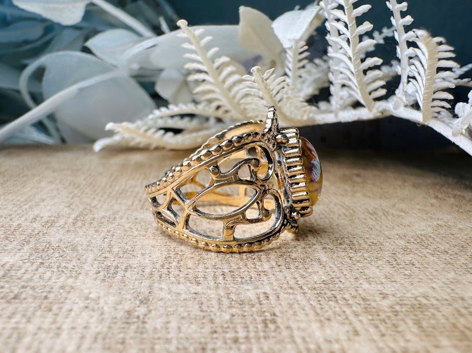 This 1970s Victorian revival vintage filigree ring is gorgeous. Featuring a faux fire opal cabochon stone set in a gold dotted bezel, the base of the ring is a beautiful open work lace filigree in an antique gold. High quality and strong filigree. Marked Sarah Coventry from 1970s.