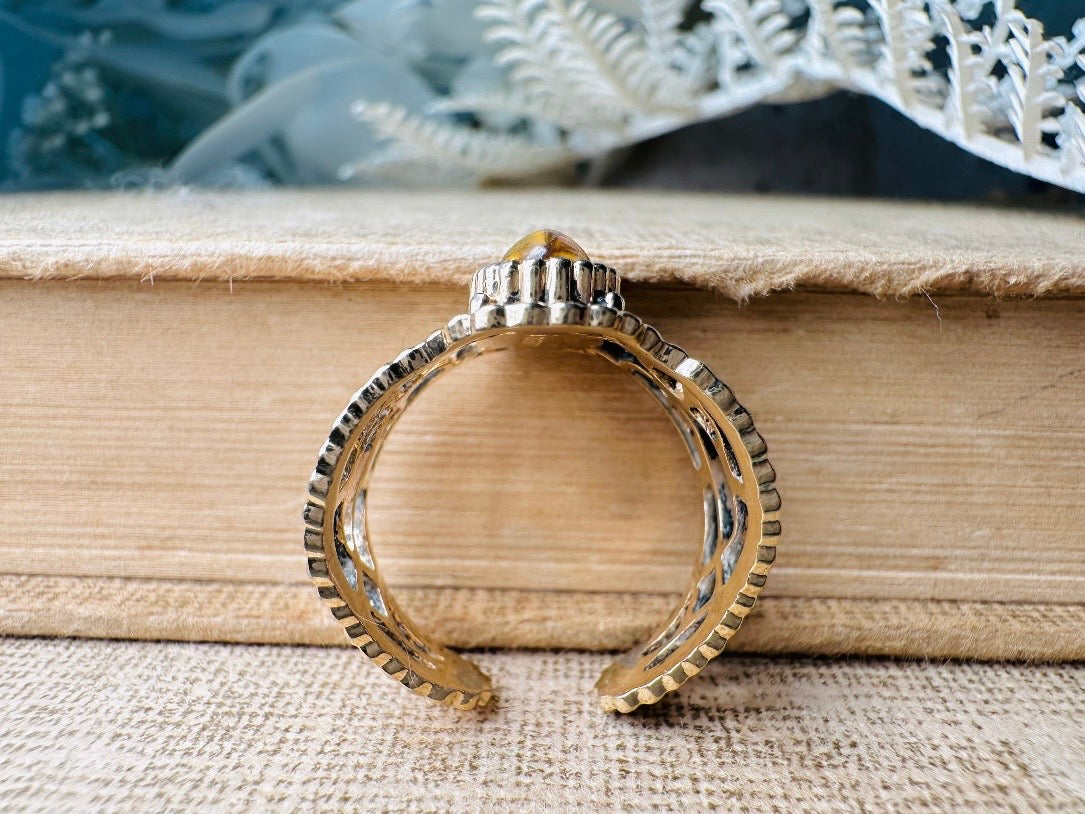 This 1970s Victorian revival vintage filigree ring is gorgeous. Featuring a faux fire opal cabochon stone set in a gold dotted bezel, the base of the ring is a beautiful open work lace filigree in an antique gold. High quality and strong filigree. Marked Sarah Coventry from 1970s.