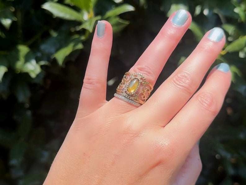 This 1970s Victorian revival vintage filigree ring is gorgeous. Featuring a faux fire opal cabochon stone set in a gold dotted bezel, the base of the ring is a beautiful open work lace filigree in an antique gold. High quality and strong filigree. Marked Sarah Coventry from 1970s.