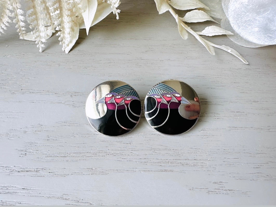 A pair of Laurel Burch vintage earrings titled "Celestial Birds". These post earrings are shiny silver with black and plum pink enamel of three birds lined up in a side profile. Laurel Burch is highly collectible, and these are so unique. Engraved with the the title "Celestial Birds" on the back of earrings along the the signature on the backs. Silver plated posts, excellent condition with very minor wear. They are about 1 inch big and available from Piggle and Pop.