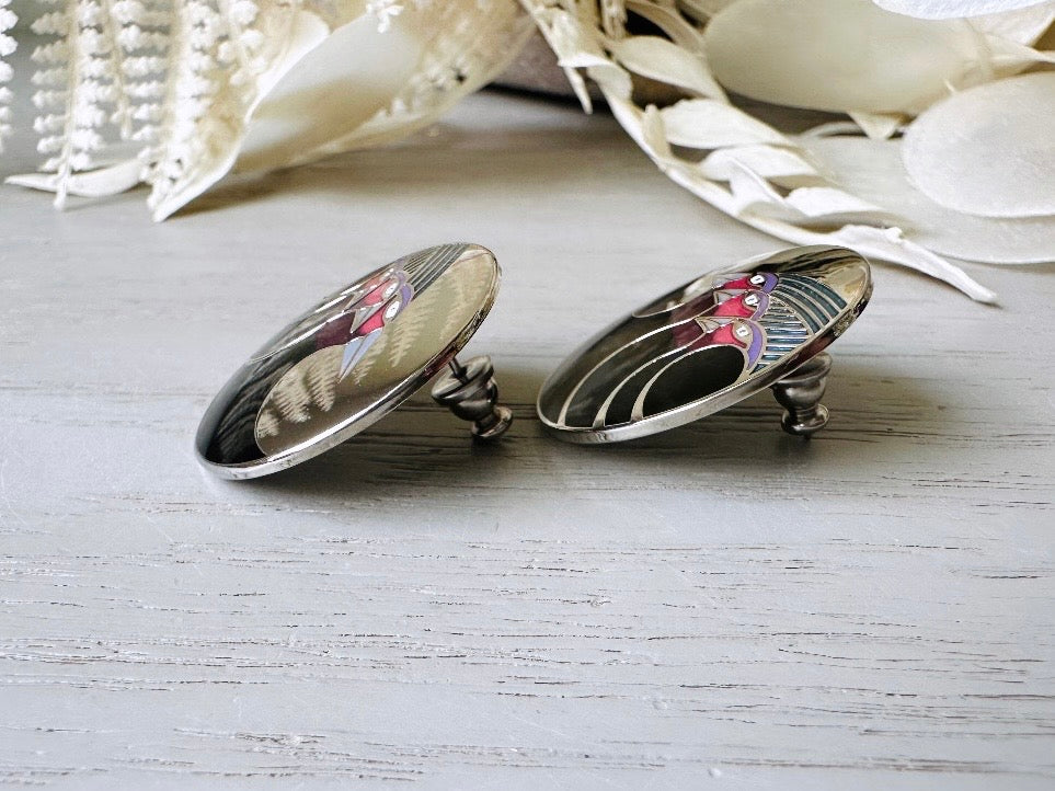 A pair of Laurel Burch vintage earrings titled "Celestial Birds". These post earrings are shiny silver with black and plum pink enamel of three birds lined up in a side profile. Laurel Burch is highly collectible, and these are so unique. Engraved with the the title "Celestial Birds" on the back of earrings along the the signature on the backs. Silver plated posts, excellent condition with very minor wear. They are about 1 inch big and available from Piggle and Pop. Side view of earring.