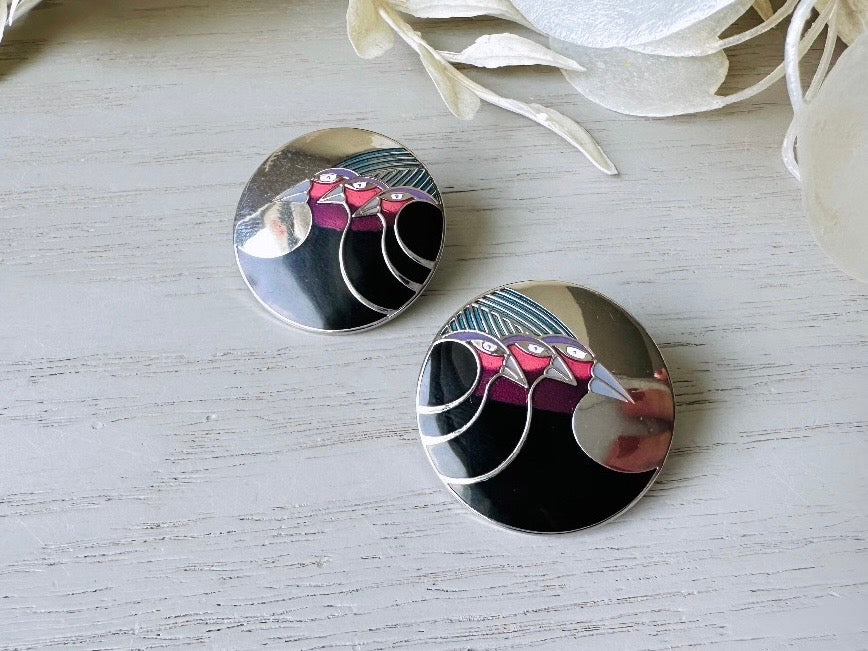 A pair of Laurel Burch vintage earrings titled "Celestial Birds". These post earrings are shiny silver with black and plum pink enamel of three birds lined up in a side profile. Laurel Burch is highly collectible, and these are so unique. Engraved with the the title "Celestial Birds" on the back of earrings along the the signature on the backs. Silver plated posts, excellent condition with very minor wear. They are about 1 inch big and available from Piggle and Pop.