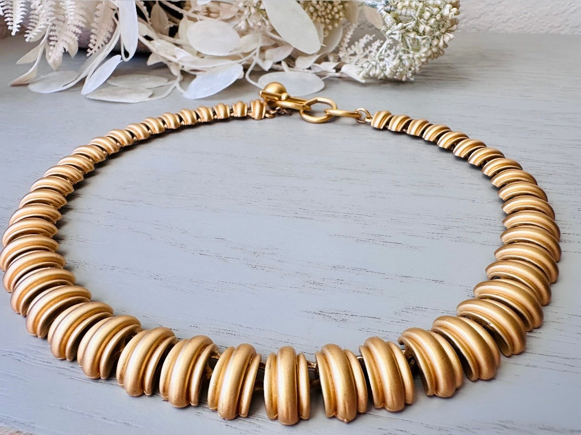 This vintage Anne Klein matte gold statement necklace is a beautiful classic satin gold collar necklace with articulated link segments.A signed AK piece, well known for superior quality and craftsmanship- this gold collar necklace is the perfect one to wear alone or pair with others for a spectacular stack. Toggle clasp at adjustable lengths.