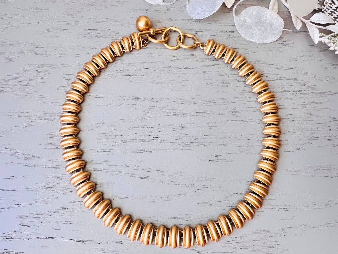 This vintage Anne Klein matte gold statement necklace is a beautiful classic satin gold collar necklace with articulated link segments.A signed AK piece, well known for superior quality and craftsmanship- this gold collar necklace is the perfect one to wear alone or pair with others for a spectacular stack. Toggle clasp at adjustable lengths. top view.