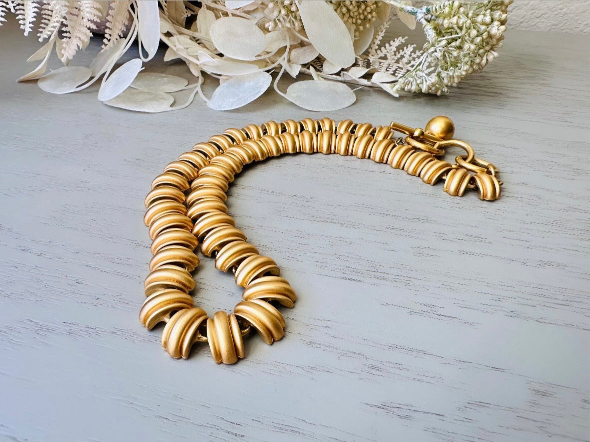 This vintage Anne Klein matte gold statement necklace is a beautiful classic satin gold collar necklace with articulated link segments.A signed AK piece, well known for superior quality and craftsmanship- this gold collar necklace is the perfect one to wear alone or pair with others for a spectacular stack. Toggle clasp at adjustable lengths.