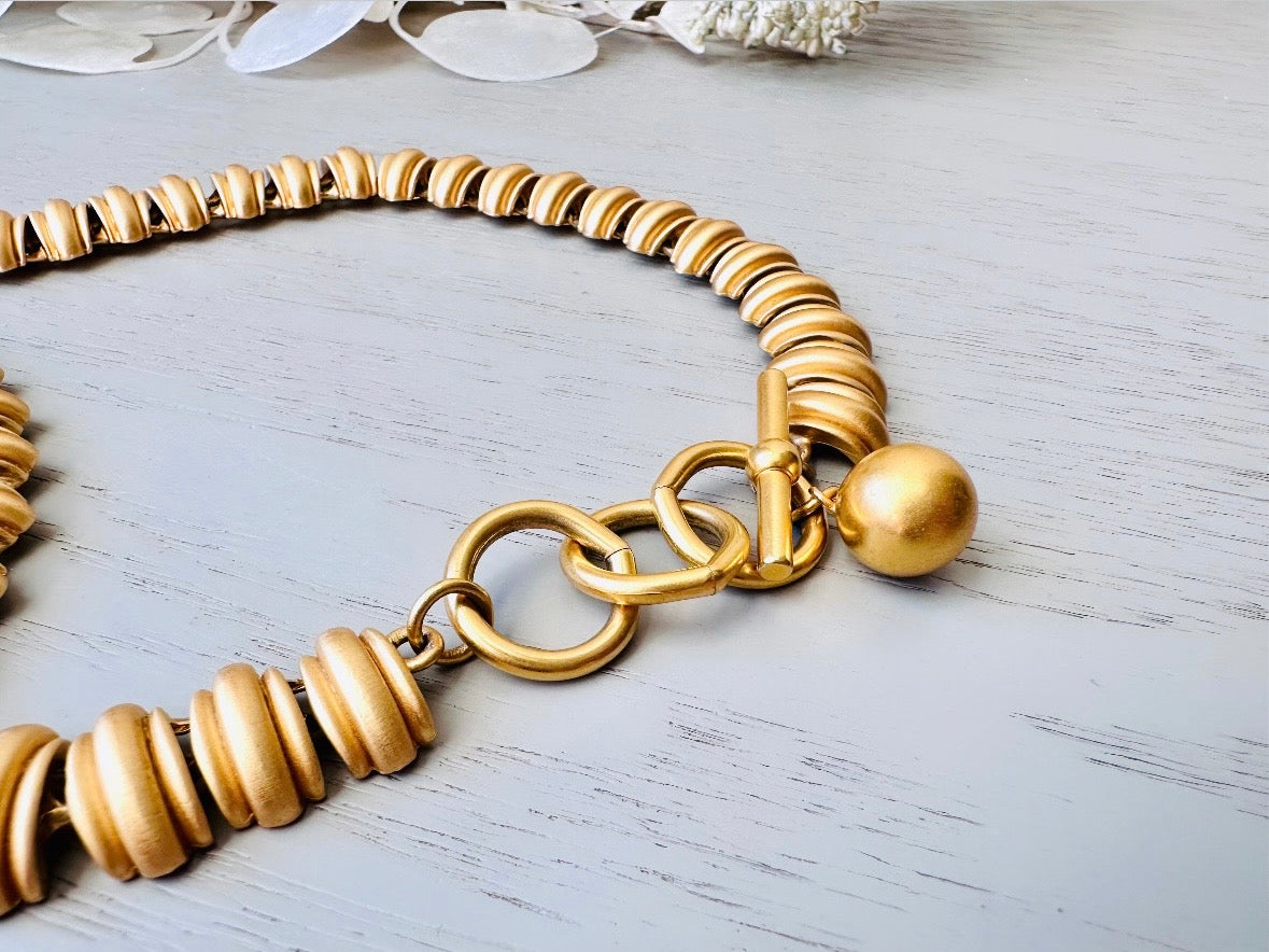 This vintage Anne Klein matte gold statement necklace is a beautiful classic satin gold collar necklace with articulated link segments.A signed AK piece, well known for superior quality and craftsmanship- this gold collar necklace is the perfect one to wear alone or pair with others for a spectacular stack. Toggle clasp at adjustable lengths.
