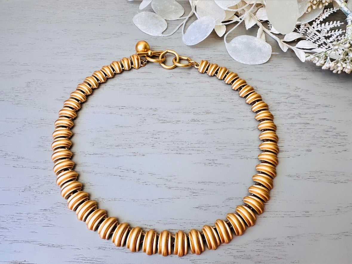 This vintage Anne Klein matte gold statement necklace is a beautiful classic satin gold collar necklace with articulated link segments.A signed AK piece, well known for superior quality and craftsmanship- this gold collar necklace is the perfect one to wear alone or pair with others for a spectacular stack. Toggle clasp at adjustable lengths.