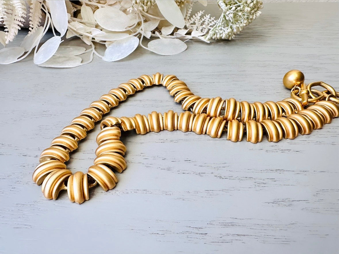 This vintage Anne Klein matte gold statement necklace is a beautiful classic satin gold collar necklace with articulated link segments.A signed AK piece, well known for superior quality and craftsmanship- this gold collar necklace is the perfect one to wear alone or pair with others for a spectacular stack. Toggle clasp at adjustable lengths. close up.