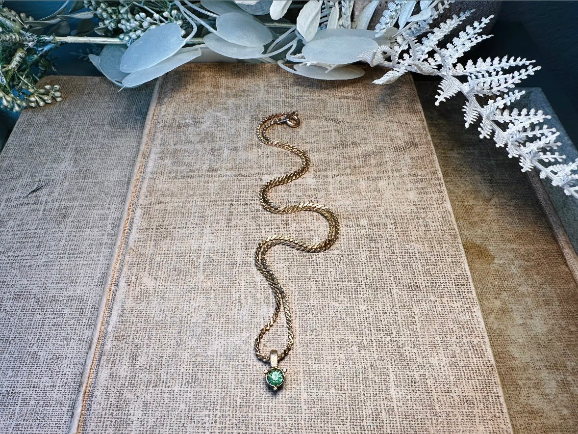 Necklace with a green pendant on a textured surface with decorative plants.