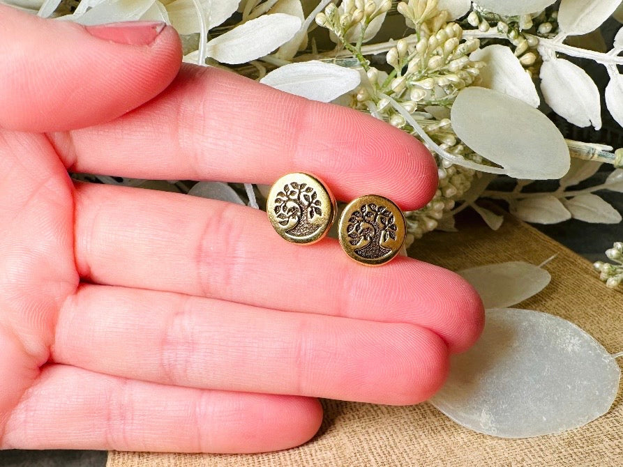 Gold tree-of-life earrings held between fingers with a floral background