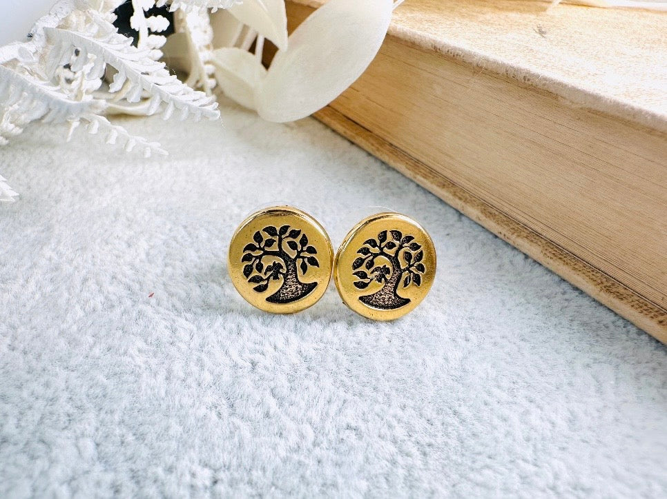 Gold tree-shaped earrings on a textured surface with a book in the background