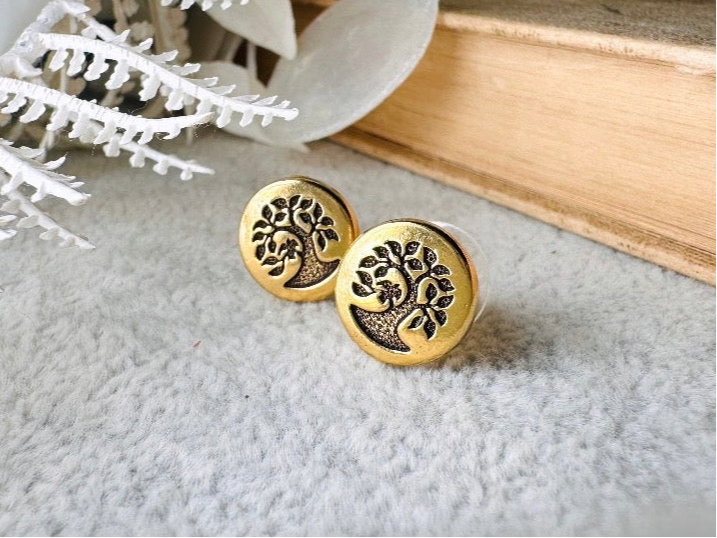 Gold tree of life earrings by Piggle and Pop on a textured surface with a book and white branches in the background