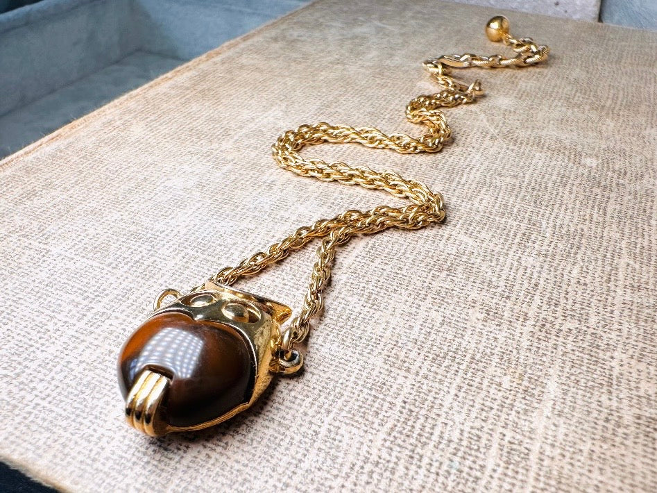 This vintage signed Crown Trifari Jelly Belly Owl necklace is a fantastic find! Gold tone twisted cable chain hosts a small intricate owl pendant with eye cut outs and a glowing chocolate brown lucite belly. These necklaces are highly collectible and hard to find with their original chains. From the 1960s. In great condition, with minimal wear from age, no major flaws to note.