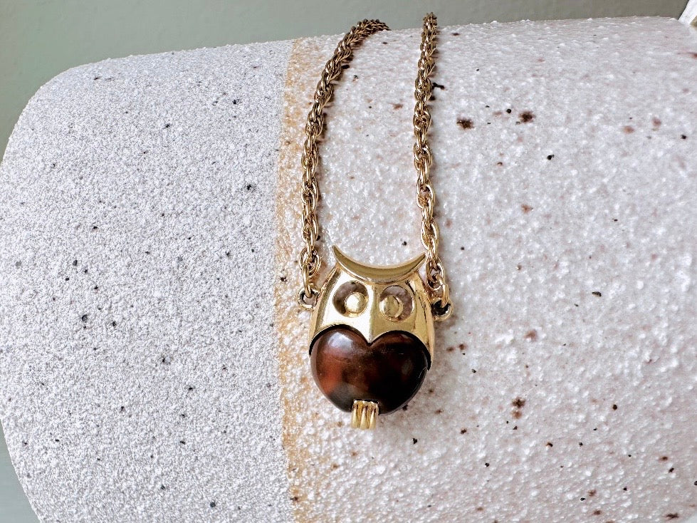This vintage signed Crown Trifari Jelly Belly Owl necklace is a fantastic find! Gold tone twisted cable chain hosts a small intricate owl pendant with eye cut outs and a glowing chocolate brown lucite belly. These necklaces are highly collectible and hard to find with their original chains. From the 1960s. In great condition, with minimal wear from age, no major flaws to note.
