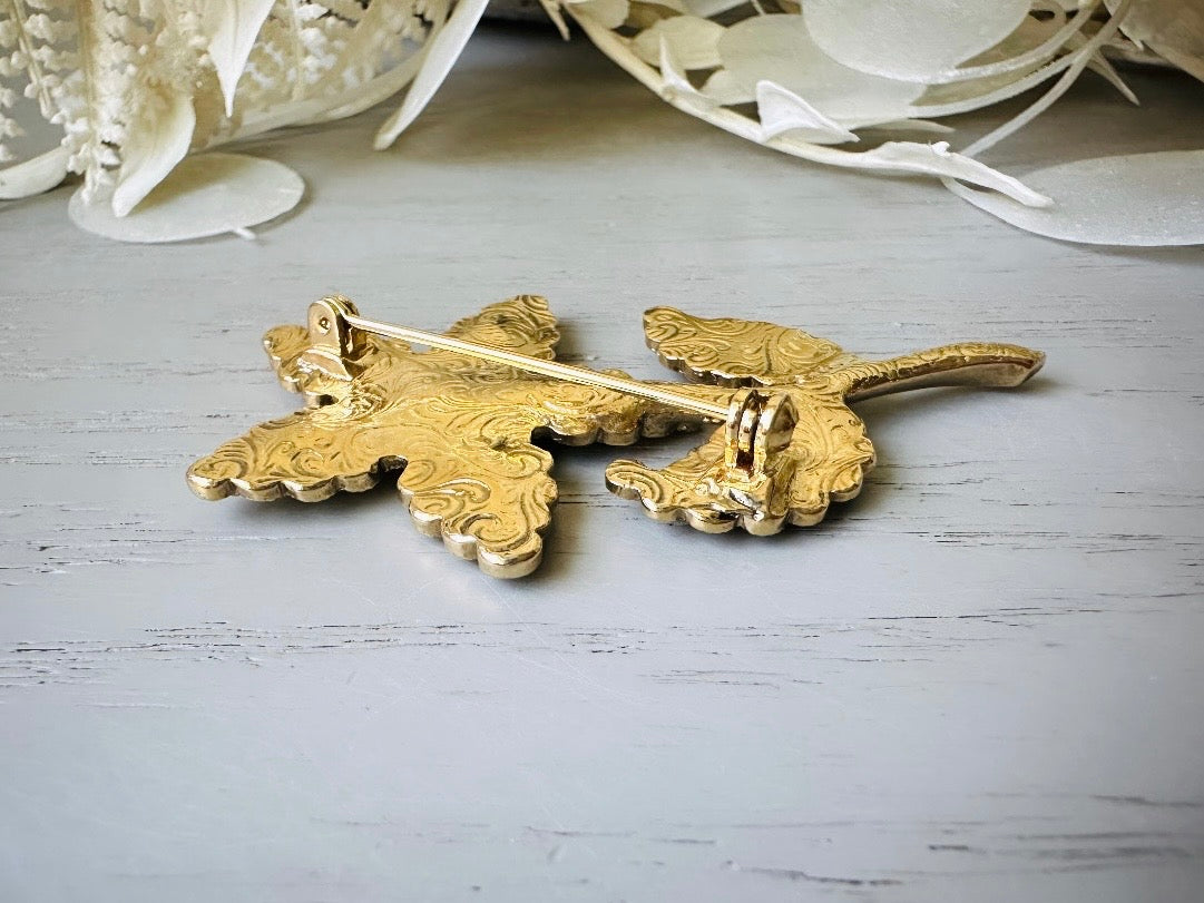 A beautiful vintage flower brooch by the brand 1928. This shows the reverse side that has the signature embossing of the 1928 brand. The brooch is on the signature background of the shop Piggle and Pop, a light gray wood table with white floral background.
