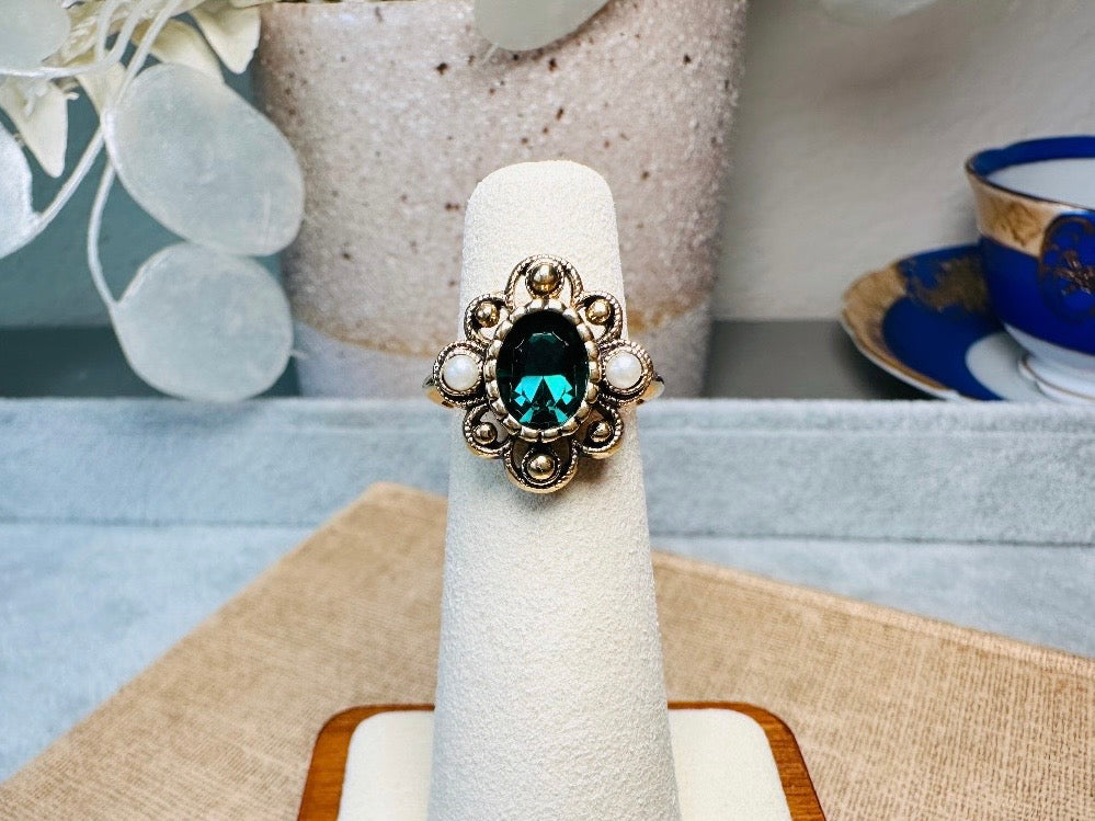 This vintage emerald green and pearl gold cocktail ring is such a pretty piece. Vintage Avon from the 1976 Versailles collection. Green, pearls and gold are a beautiful color combination. The center faceted oval green stone is surrounded in a raised filigree design that is full of vintage character, with two tiny pearl cabochon accents. Signed in excellent vintage condition. 