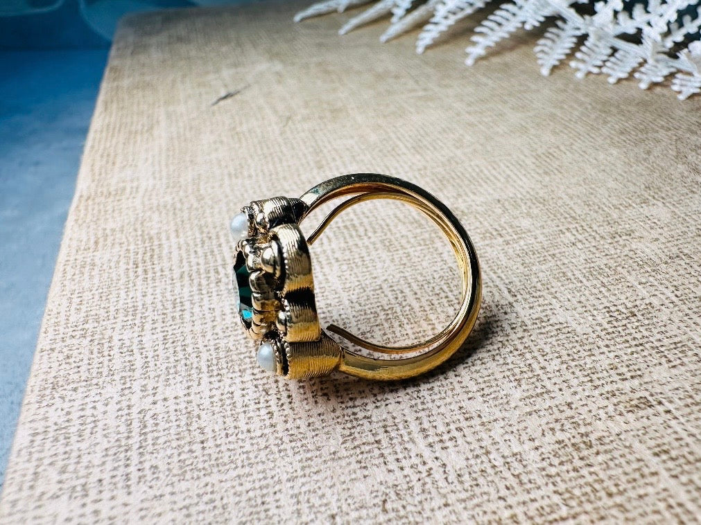 This vintage emerald green and pearl gold cocktail ring is such a pretty piece. Vintage Avon from the 1976 Versailles collection. Green, pearls and gold are a beautiful color combination. The center faceted oval green stone is surrounded in a raised filigree design that is full of vintage character, with two tiny pearl cabochon accents. Signed in excellent vintage condition. 