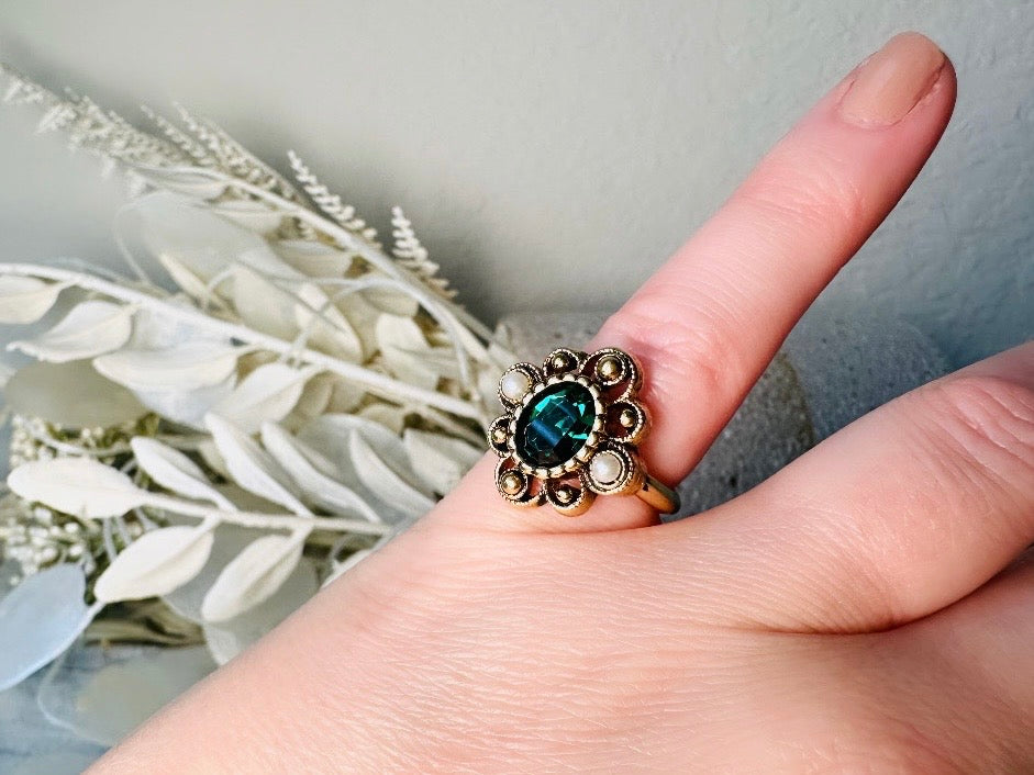 This vintage emerald green and pearl gold cocktail ring is such a pretty piece. Vintage Avon from the 1976 Versailles collection. Green, pearls and gold are a beautiful color combination. The center faceted oval green stone is surrounded in a raised filigree design that is full of vintage character, with two tiny pearl cabochon accents. Signed in excellent vintage condition. 