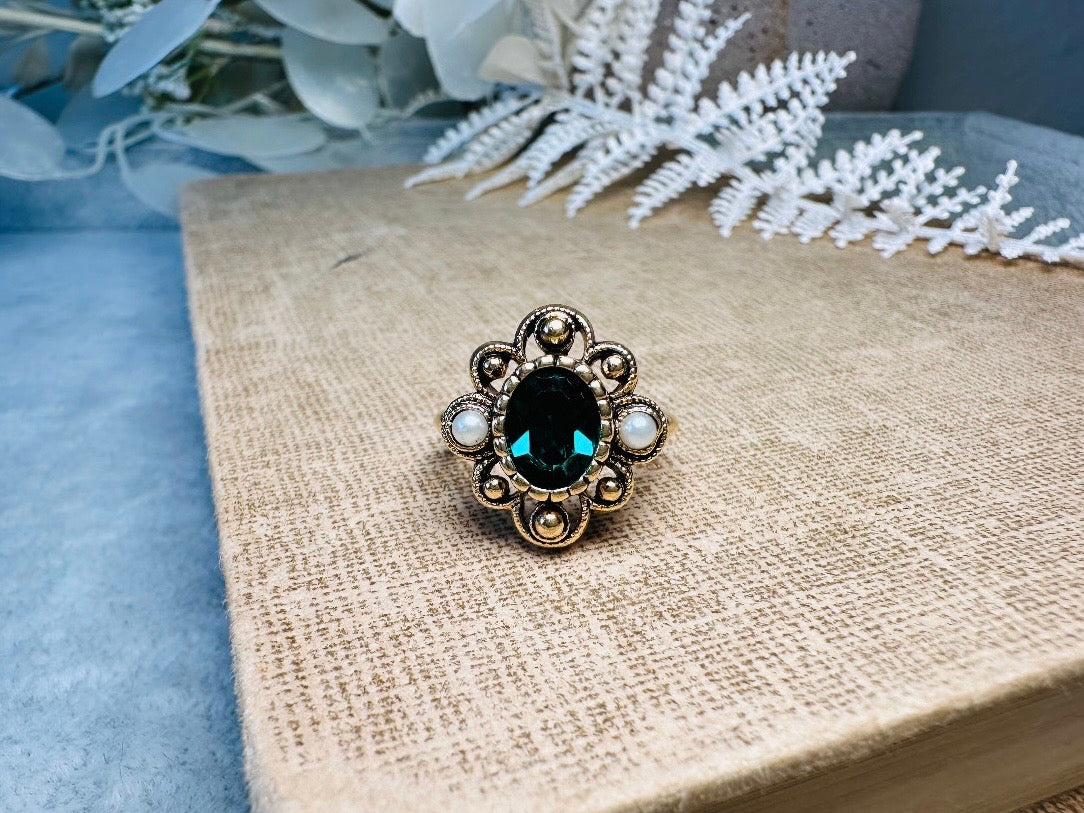 This vintage emerald green and pearl gold cocktail ring is such a pretty piece. Vintage Avon from the 1976 Versailles collection. Green, pearls and gold are a beautiful color combination. The center faceted oval green stone is surrounded in a raised filigree design that is full of vintage character, with two tiny pearl cabochon accents. Signed in excellent vintage condition. 
