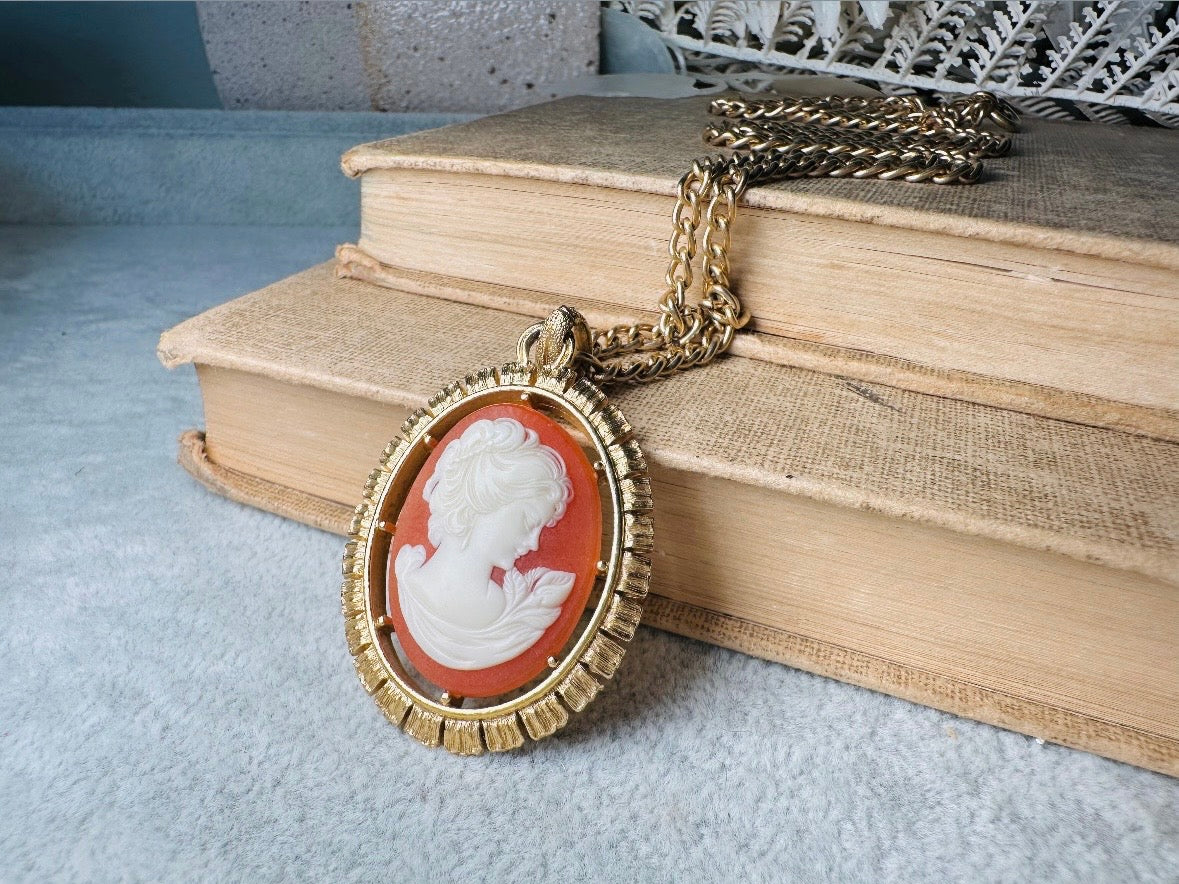 This 1970s vintage Victorian Revival cameo necklace is marvelous. Bold, yet elegant this classic necklace features a double sided reversible cameo pendant. On one side is the portrait of a lady in cream and classic muted orange and on the other side an ornate Fleur de Lis raised in gold. This vintage necklace features a medium width antique gold curb chain, from 1974. In great vintage condition please view all pics. Would look incredible in a necklace stack for a modern twist.