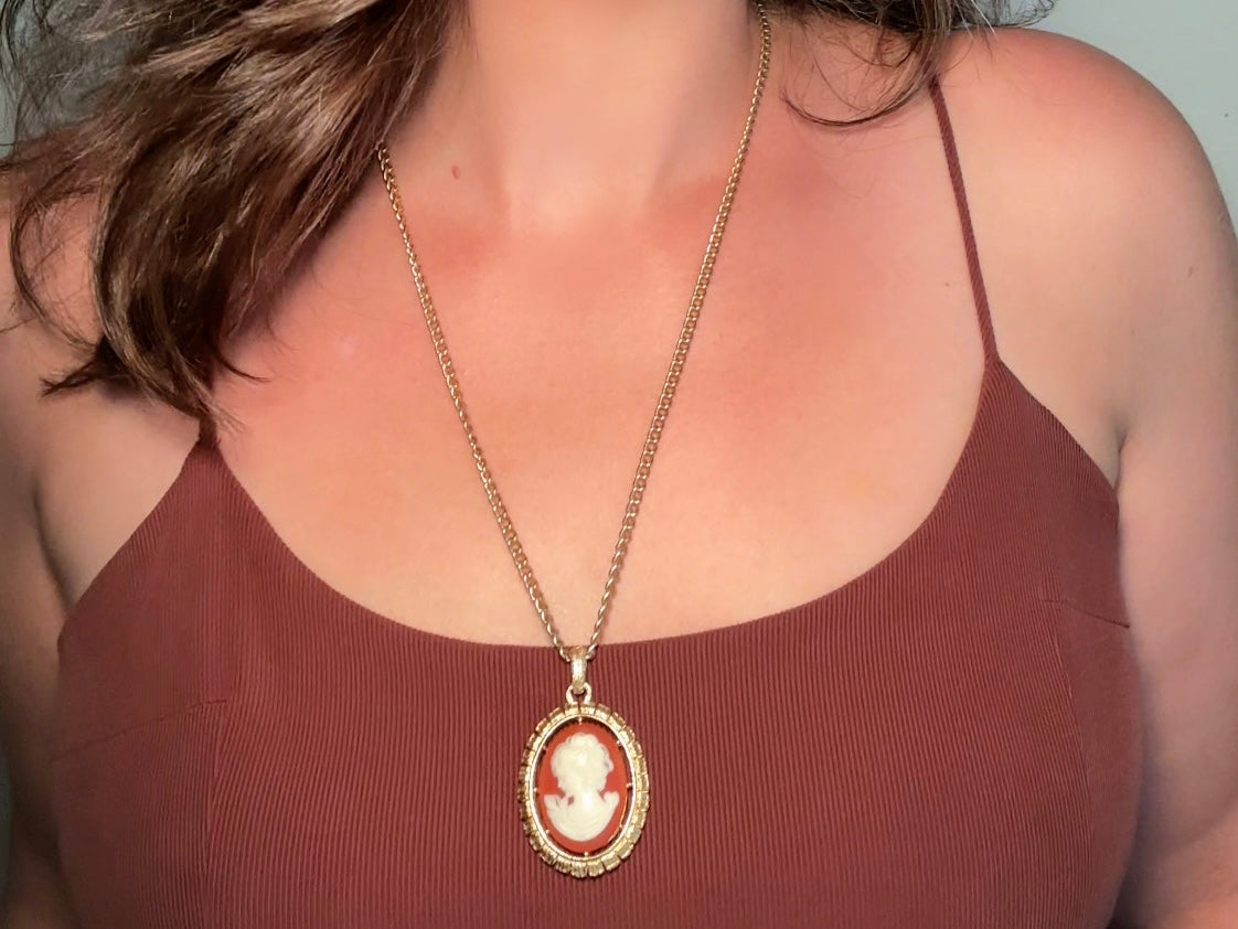 This 1970s vintage Victorian Revival cameo necklace is marvelous. Bold, yet elegant this classic necklace features a double sided reversible cameo pendant. On one side is the portrait of a lady in cream and classic muted orange and on the other side an ornate Fleur de Lis raised in gold. This vintage necklace features a medium width antique gold curb chain, from 1974. In great vintage condition please view all pics. Would look incredible in a necklace stack for a modern twist.