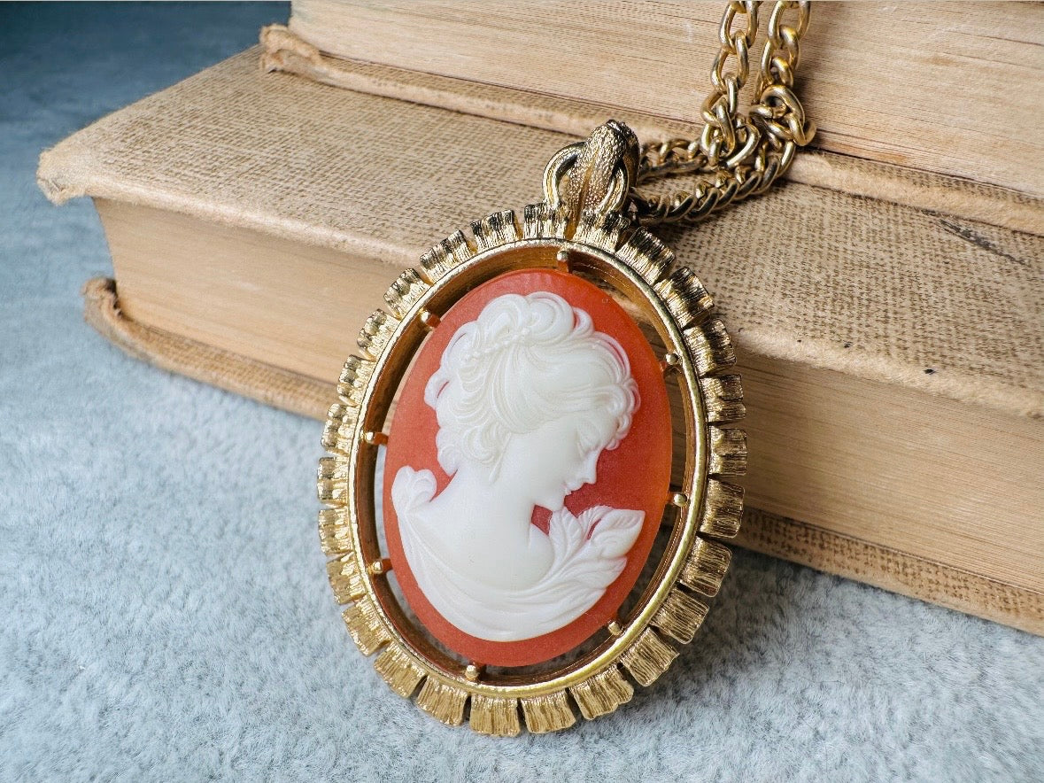This 1970s vintage Victorian Revival cameo necklace is marvelous. Bold, yet elegant this classic necklace features a double sided reversible cameo pendant. On one side is the portrait of a lady in cream and classic muted orange and on the other side an ornate Fleur de Lis raised in gold. This vintage necklace features a medium width antique gold curb chain, from 1974. In great vintage condition please view all pics. Would look incredible in a necklace stack for a modern twist.
