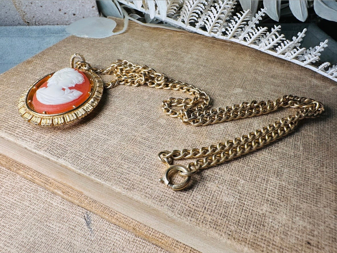 This 1970s vintage Victorian Revival cameo necklace is marvelous. Bold, yet elegant this classic necklace features a double sided reversible cameo pendant. On one side is the portrait of a lady in cream and classic muted orange and on the other side an ornate Fleur de Lis raised in gold. This vintage necklace features a medium width antique gold curb chain, from 1974. In great vintage condition please view all pics. Would look incredible in a necklace stack for a modern twist.