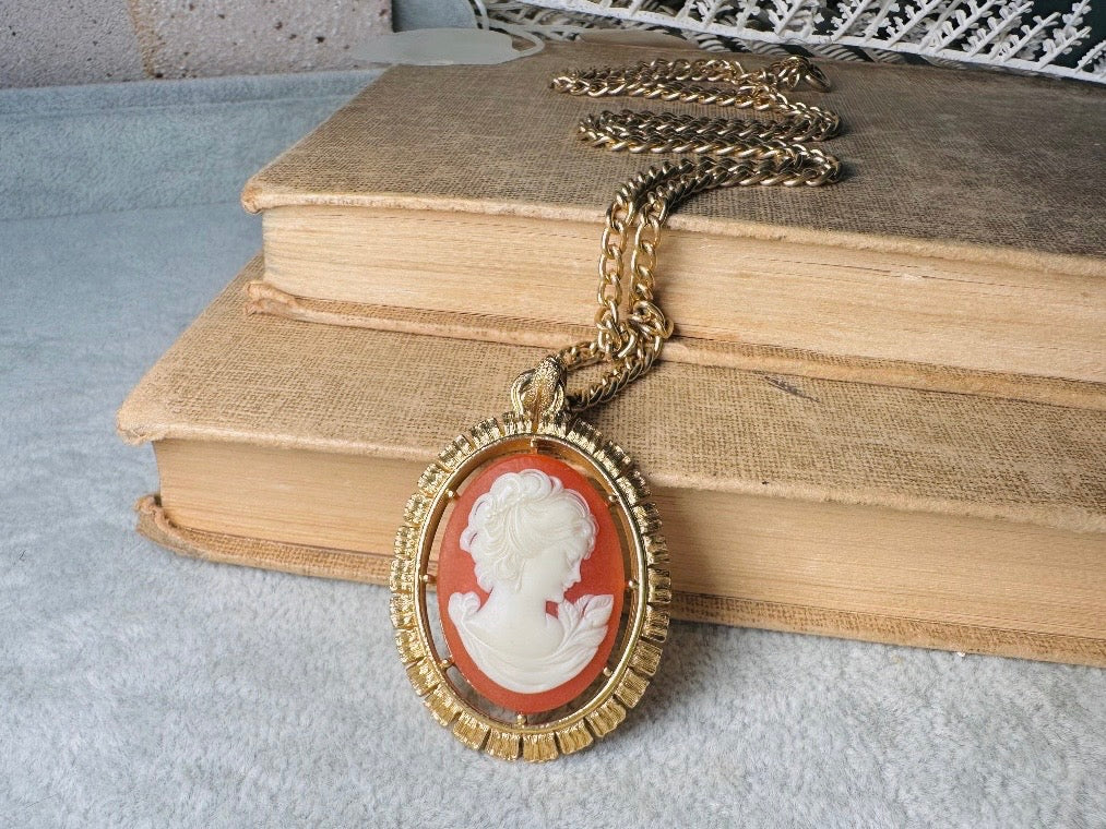 This 1970s vintage Victorian Revival cameo necklace is marvelous. Bold, yet elegant this classic necklace features a double sided reversible cameo pendant. On one side is the portrait of a lady in cream and classic muted orange and on the other side an ornate Fleur de Lis raised in gold. This vintage necklace features a medium width antique gold curb chain, from 1974. In great vintage condition please view all pics. Would look incredible in a necklace stack for a modern twist.