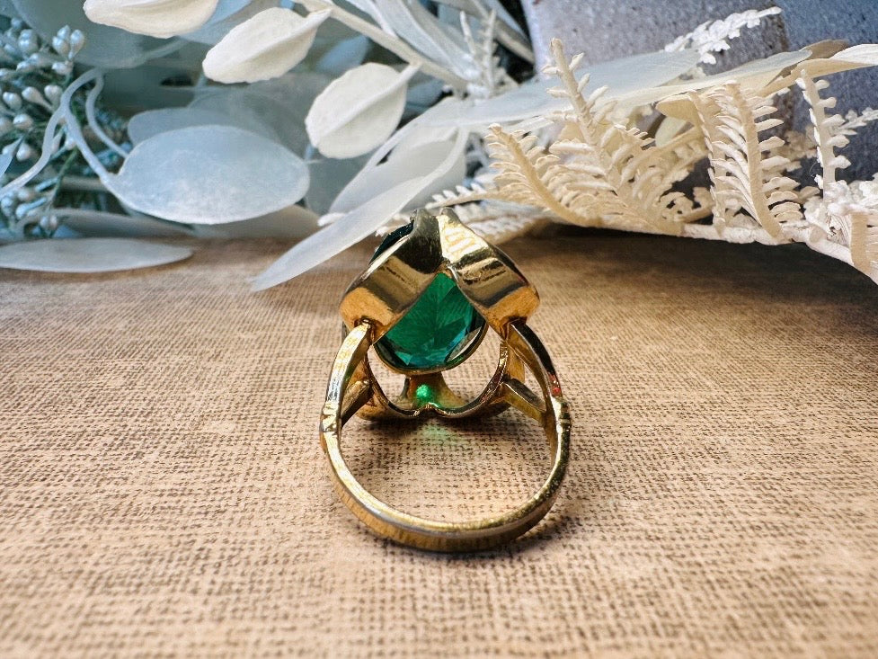 Gold ring with a green gemstone on a textured surface with decorative elements.