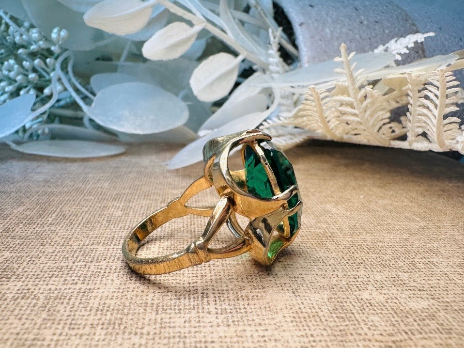 Gold ring with a green gemstone on a textured surface with decorative elements.