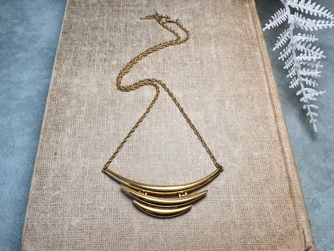 This vintage Crown Trifari triple gold bar necklace is a beauty. From the 1960s this dainty short style choker necklace looks beautiful alone or paired with others for a fantastic stack. The fine gold plated chain suspends a small gold pendant composed of 3 curved bars in graduated size- signed on back and with the signature Trifari hang tag.