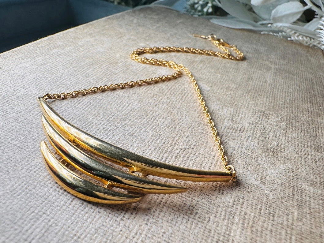 This vintage Crown Trifari triple gold bar necklace is a beauty. From the 1960s this dainty short style choker necklace looks beautiful alone or paired with others for a fantastic stack. The fine gold plated chain suspends a small gold pendant composed of 3 curved bars in graduated size- signed on back and with the signature Trifari hang tag.