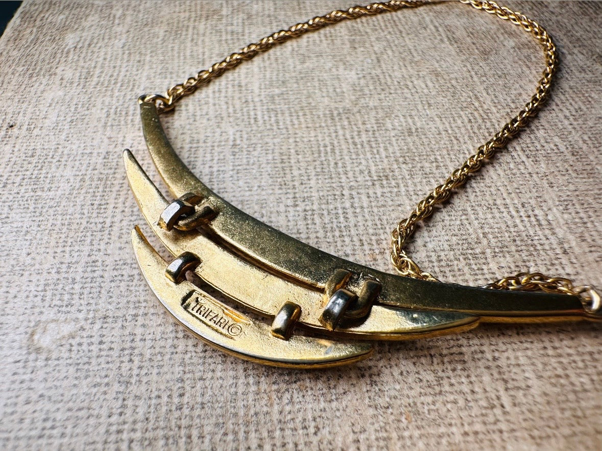 This vintage Crown Trifari triple gold bar necklace is a beauty. From the 1960s this dainty short style choker necklace looks beautiful alone or paired with others for a fantastic stack. The fine gold plated chain suspends a small gold pendant composed of 3 curved bars in graduated size- signed on back and with the signature Trifari hang tag.