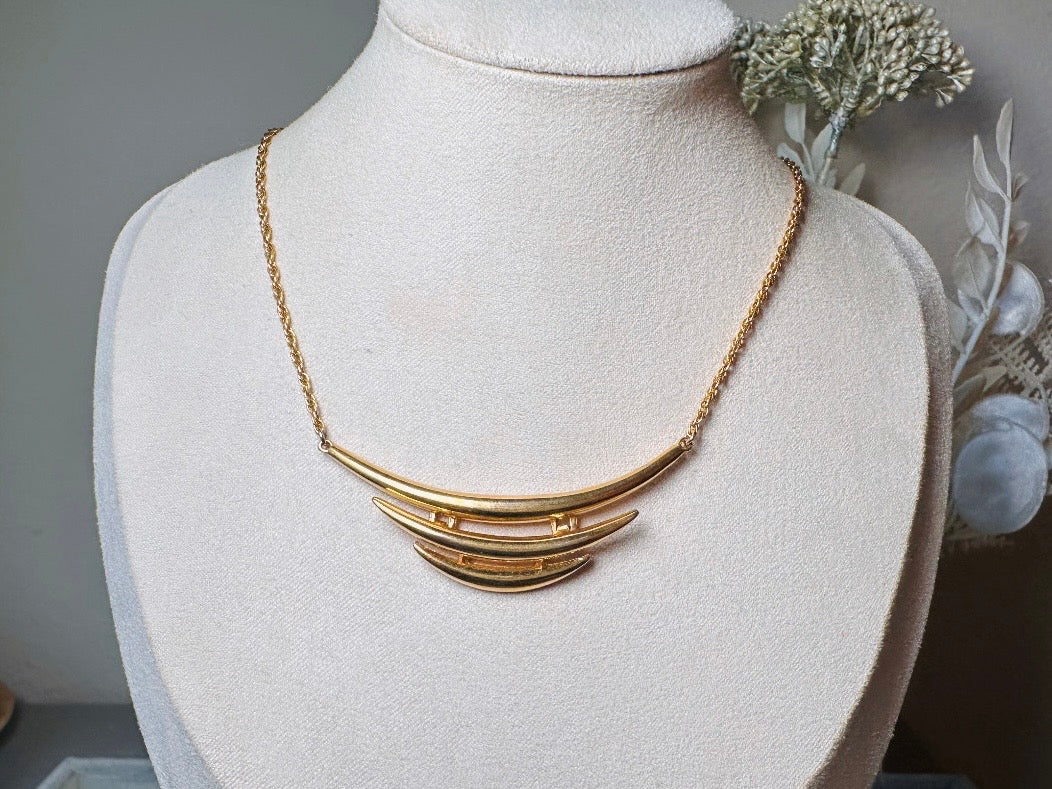 This vintage Crown Trifari triple gold bar necklace is a beauty. From the 1960s this dainty short style choker necklace looks beautiful alone or paired with others for a fantastic stack. The fine gold plated chain suspends a small gold pendant composed of 3 curved bars in graduated size- signed on back and with the signature Trifari hang tag.