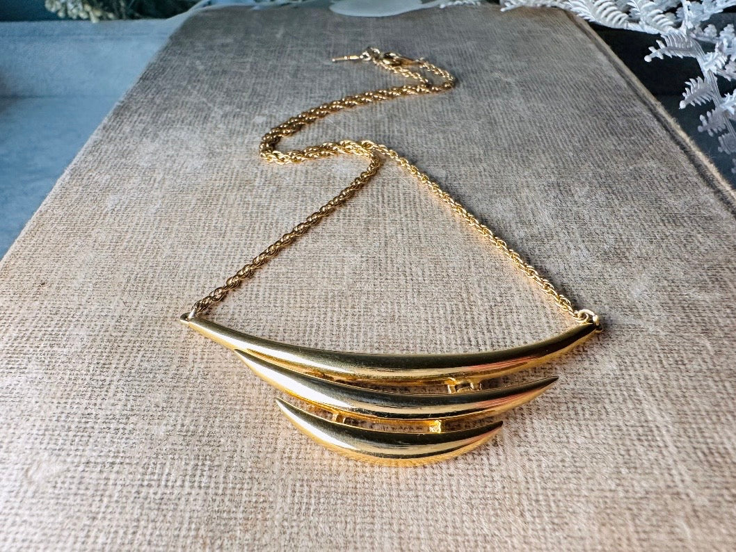 This vintage Crown Trifari triple gold bar necklace is a beauty. From the 1960s this dainty short style choker necklace looks beautiful alone or paired with others for a fantastic stack. The fine gold plated chain suspends a small gold pendant composed of 3 curved bars in graduated size- signed on back and with the signature Trifari hang tag.
